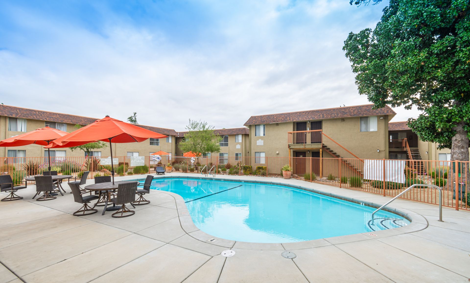 A large swimming pool with umbrellas and tables in front of a building.