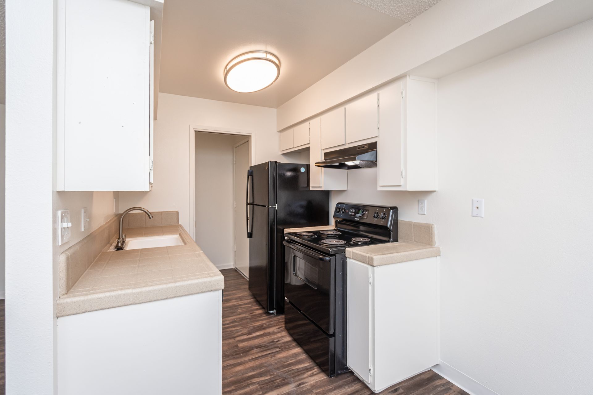 A kitchen with white cabinets , a black refrigerator , a black stove , and a sink.
