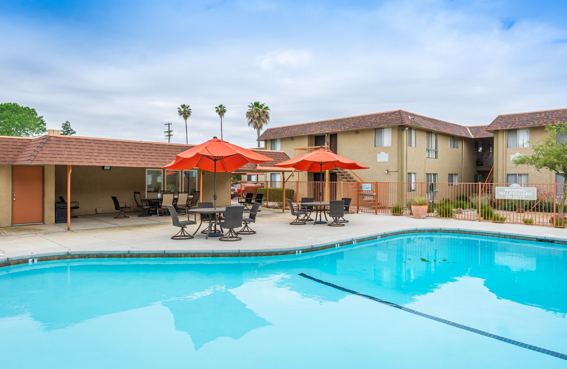 A large swimming pool with tables and umbrellas in front of a building.