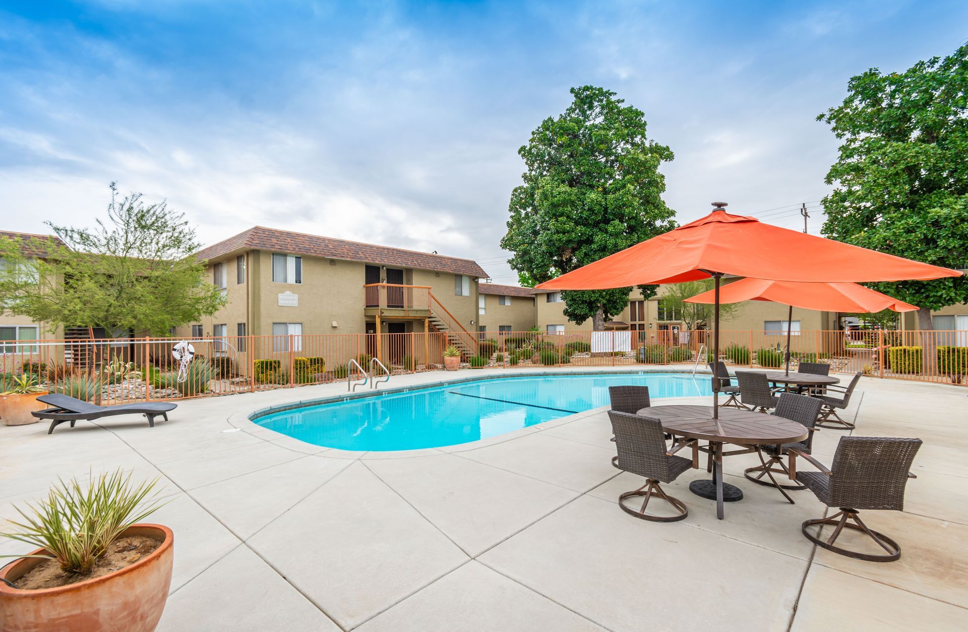 A swimming pool with tables and chairs and umbrellas in front of a building.