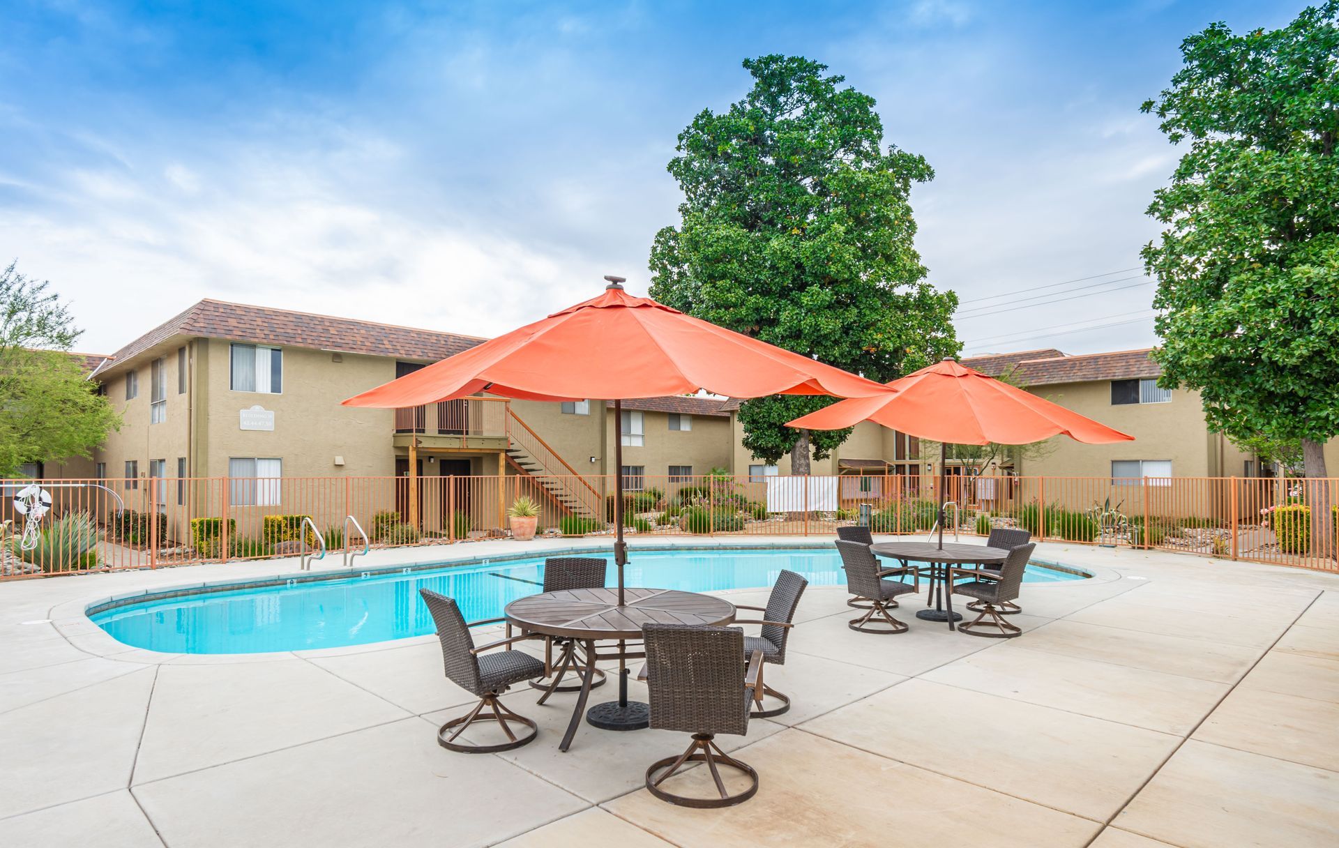 A swimming pool with tables and chairs under orange umbrellas
