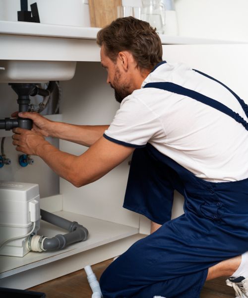A man in blue overalls is fixing a sink