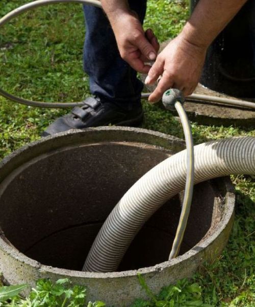 A man is using a hose to pump water into a septic tank.