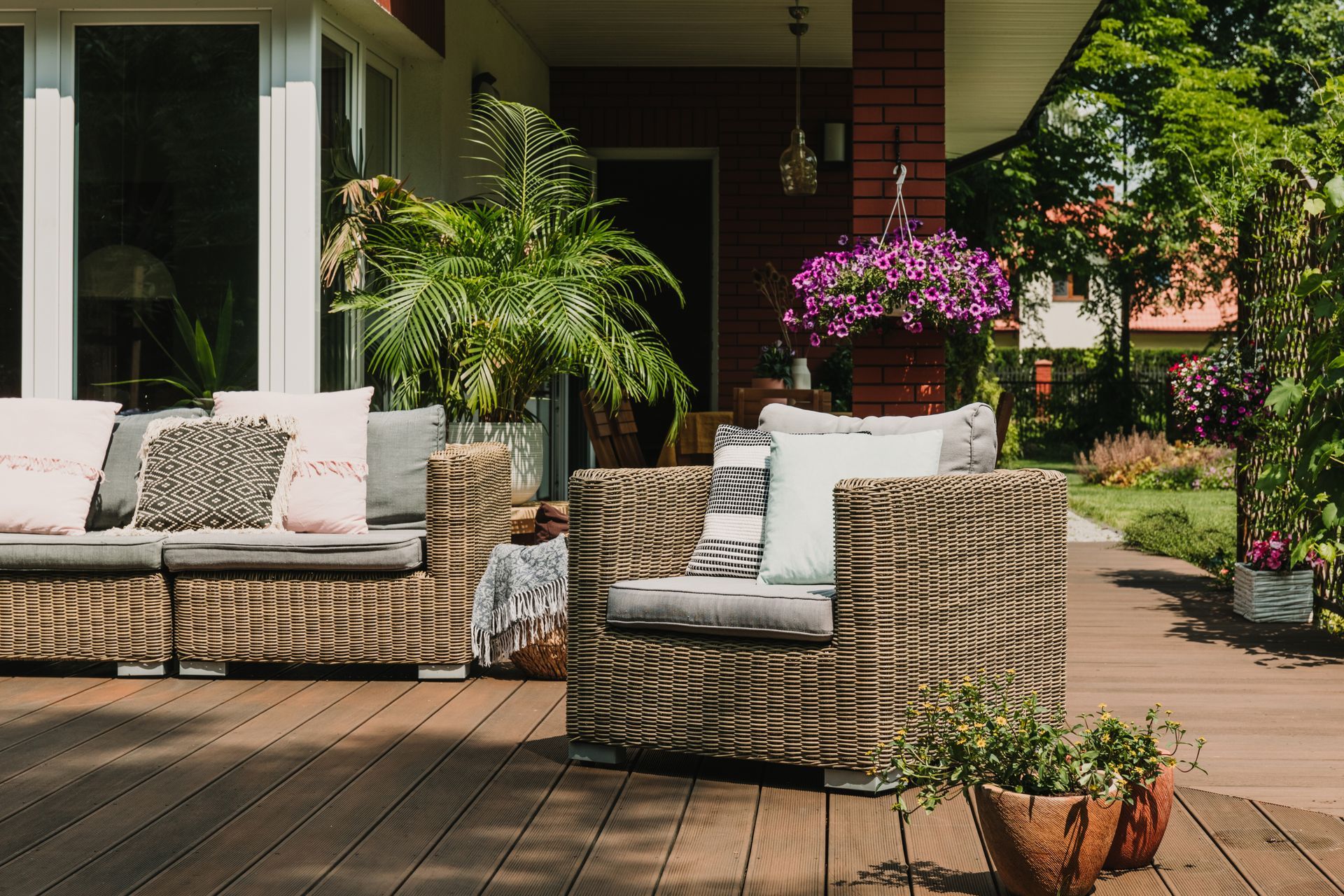 Patio furniture on a wooden deck, with potted plants and colorful flowers.
