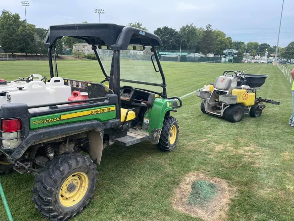 Green John Deere utility vehicle pulling a seeding machine on a grass field.
