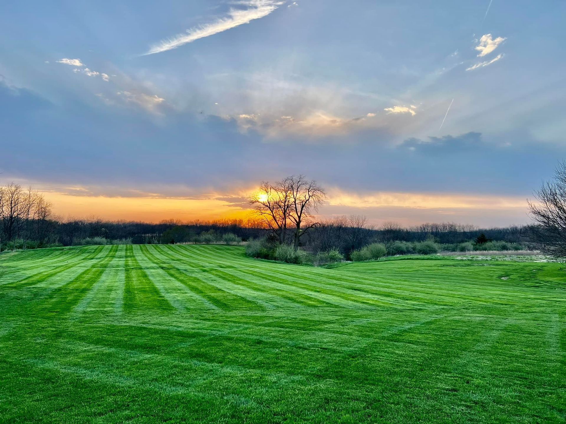 Two workers installing landscaping fabric near a house with a porch and a large rock in a garden bed.