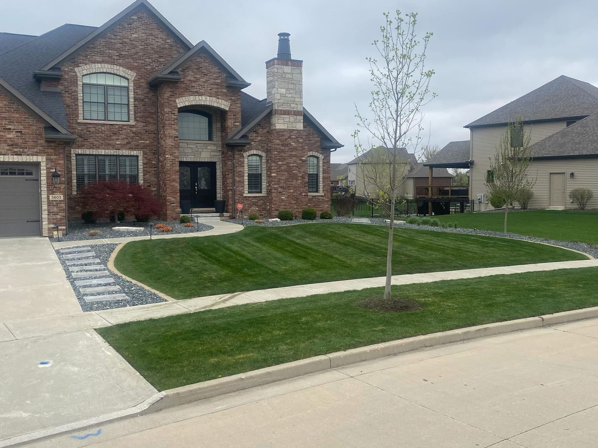 Brick house with manicured lawn, path, and small tree. Overcast sky.