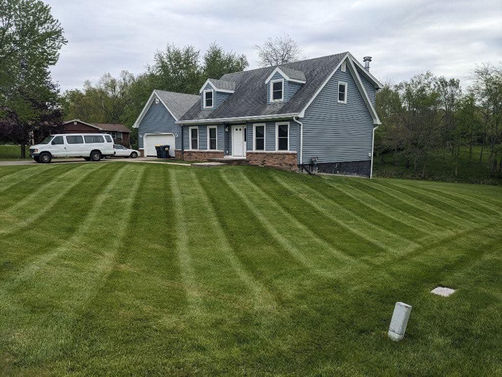 Blue house with a neatly striped green lawn. A white van is parked in the driveway. Overcast sky.