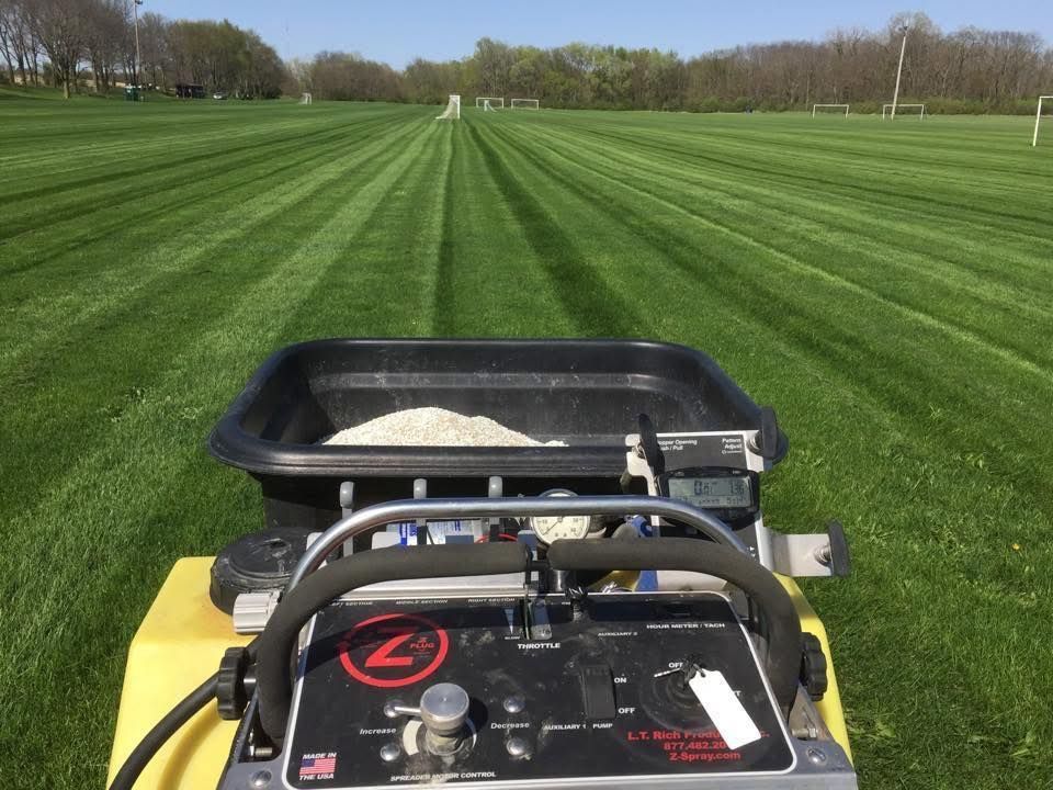 Wheelbarrow filled with weeds and gardening tool on green grass.
