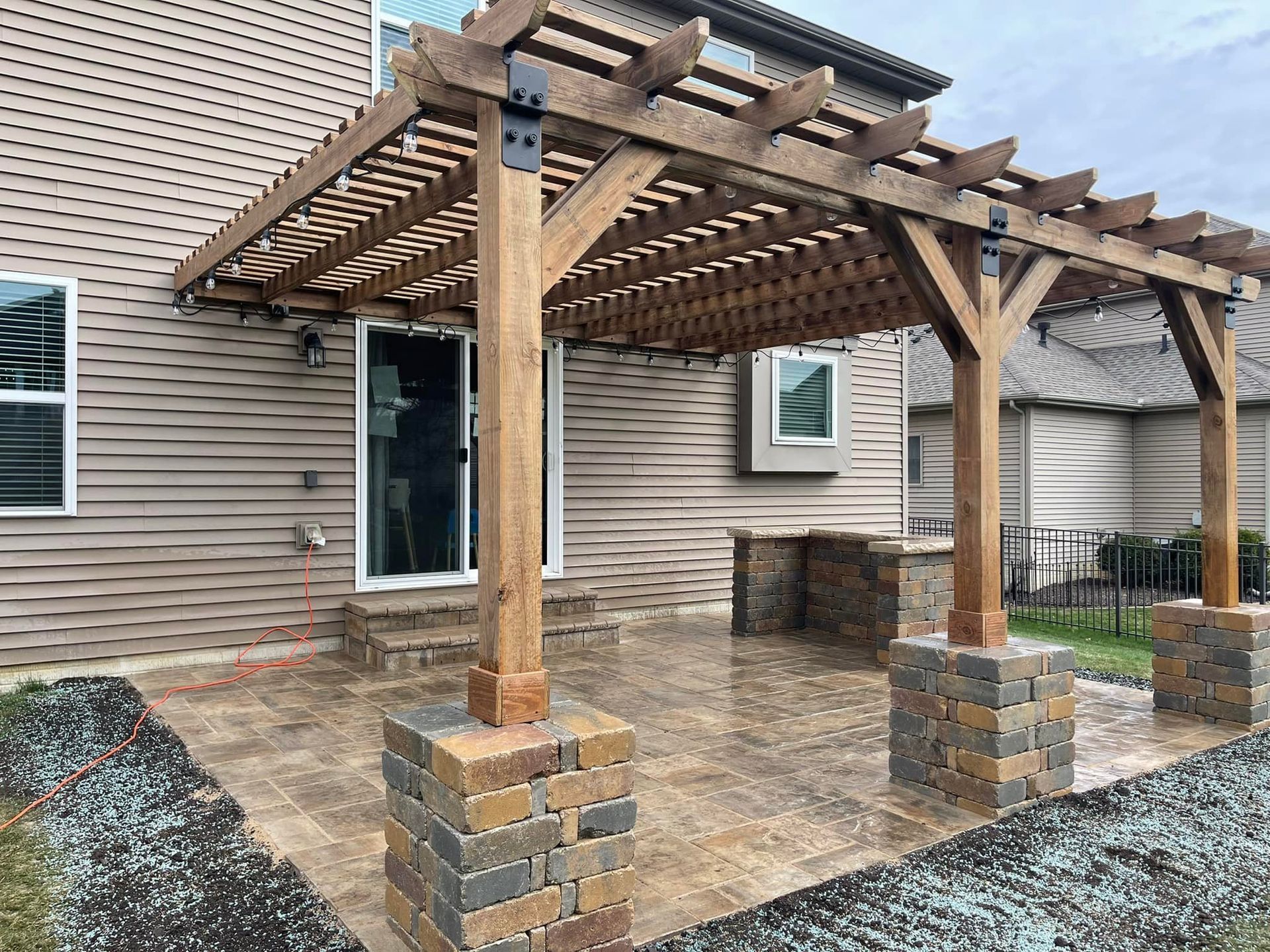 Wooden pergola over brick patio outside a beige house.