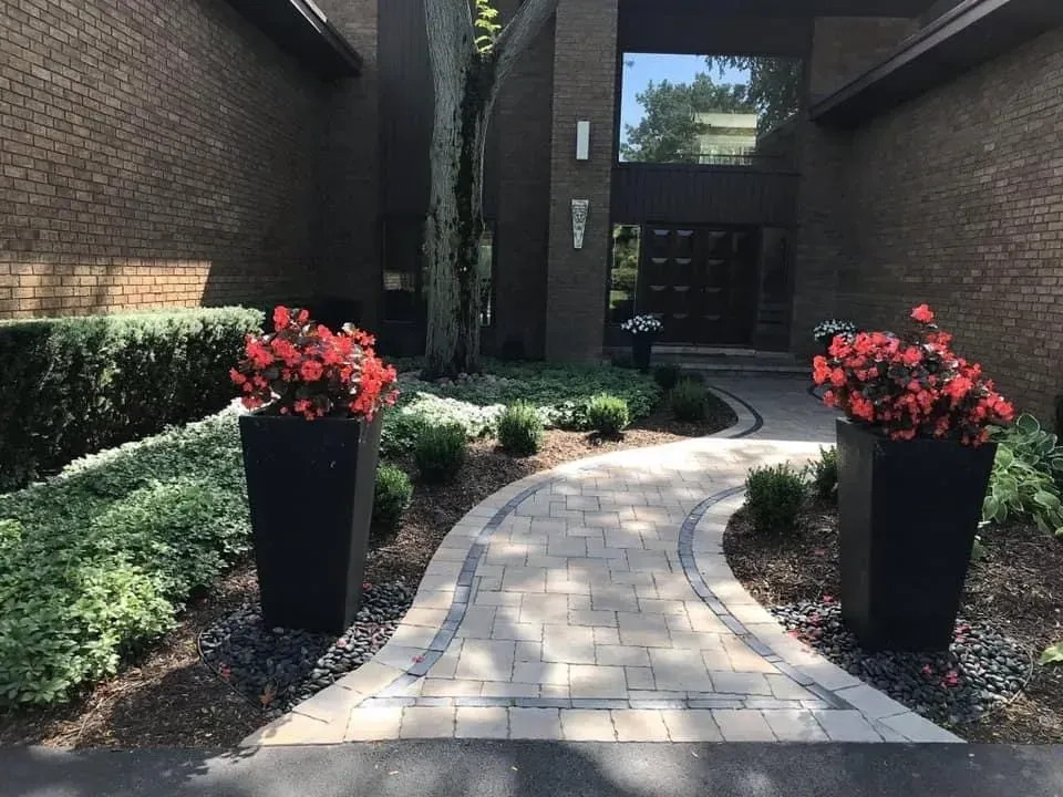 Brick house entrance with a paved path, flower planters, and landscaping.