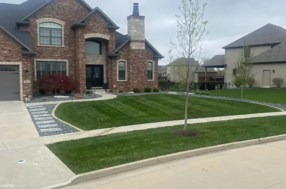 Brick house with manicured lawn, path, and small tree. Overcast sky.