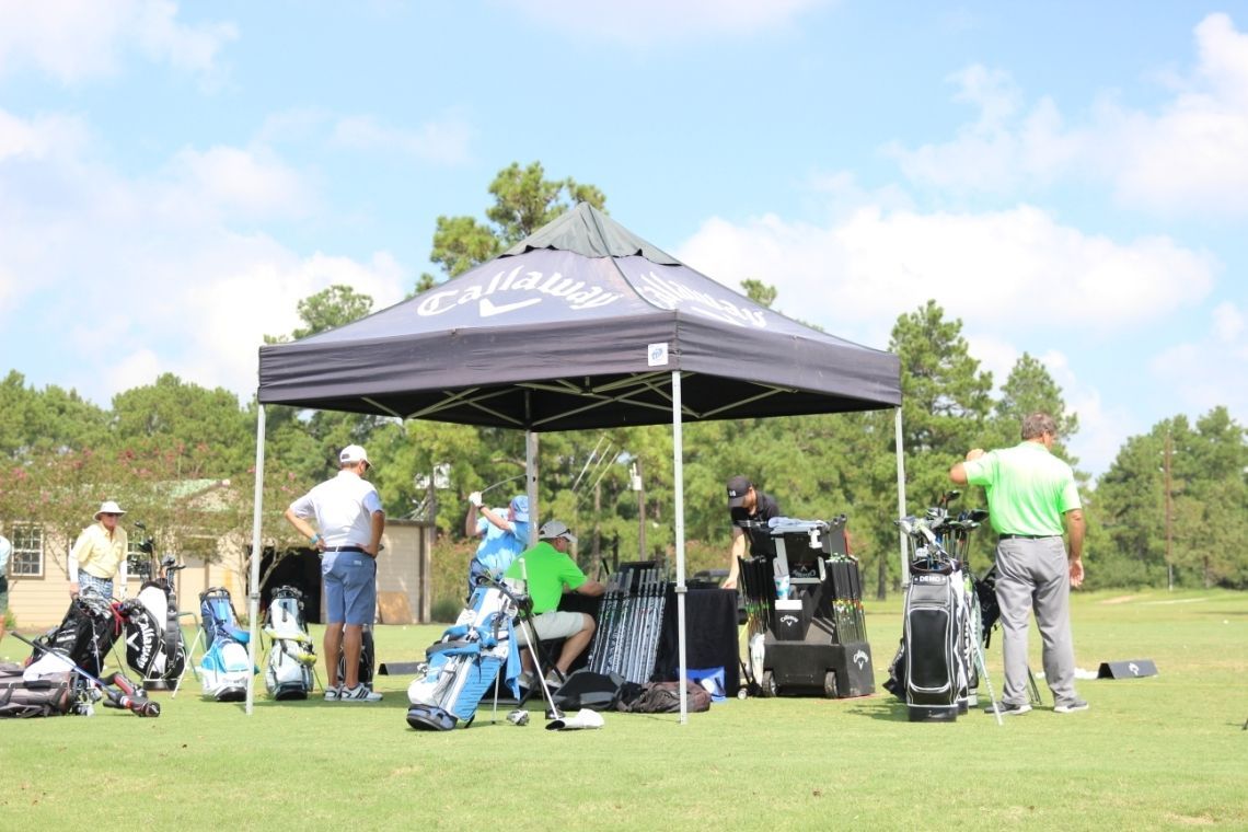 A group of people are standing under a canopy on a golf course.