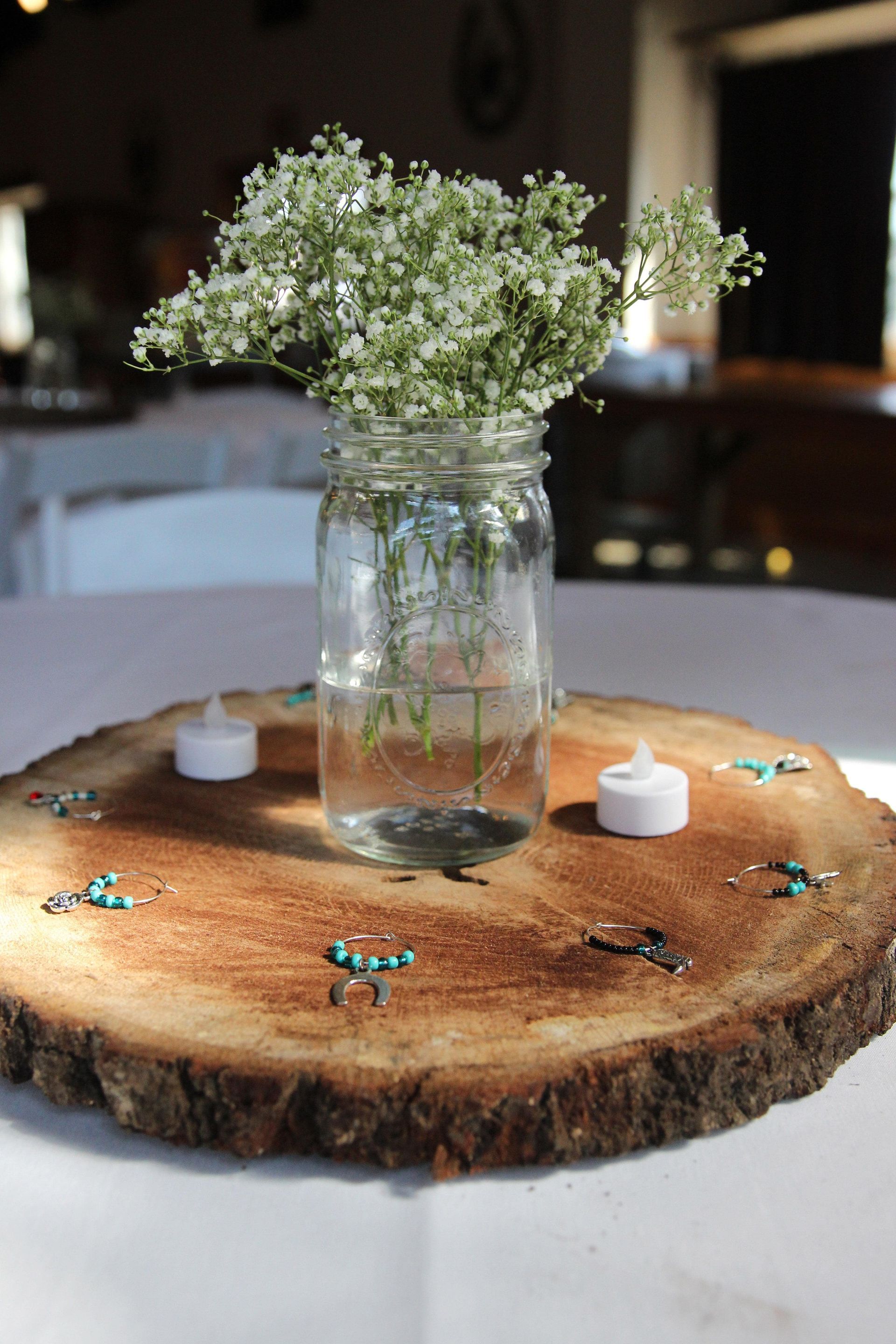 A mason jar filled with baby 's breath is sitting on a wooden slice on a table.