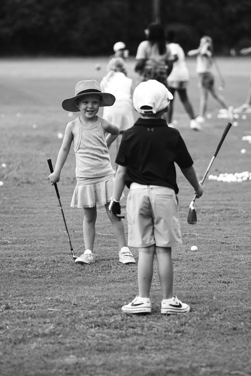 A boy and a girl are standing on a golf course holding golf clubs.