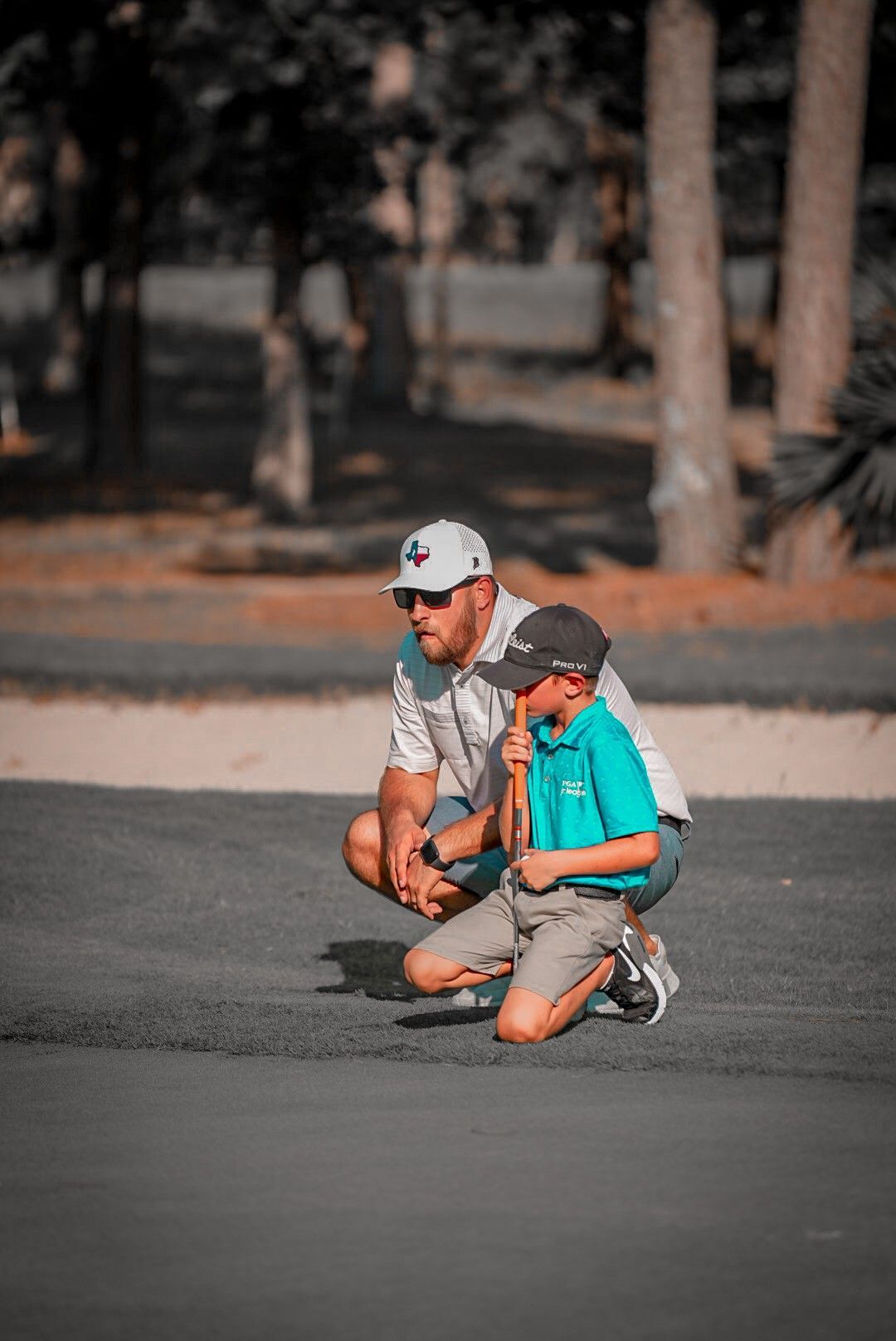 A man and a boy are kneeling down on a golf course.