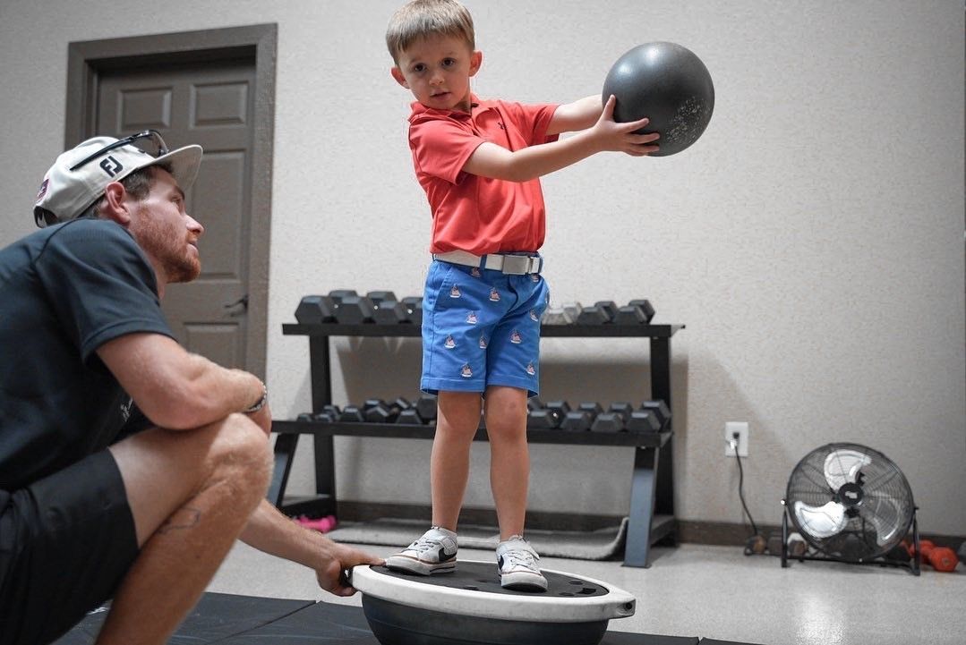 A young boy is holding a ball while standing on a balance board.