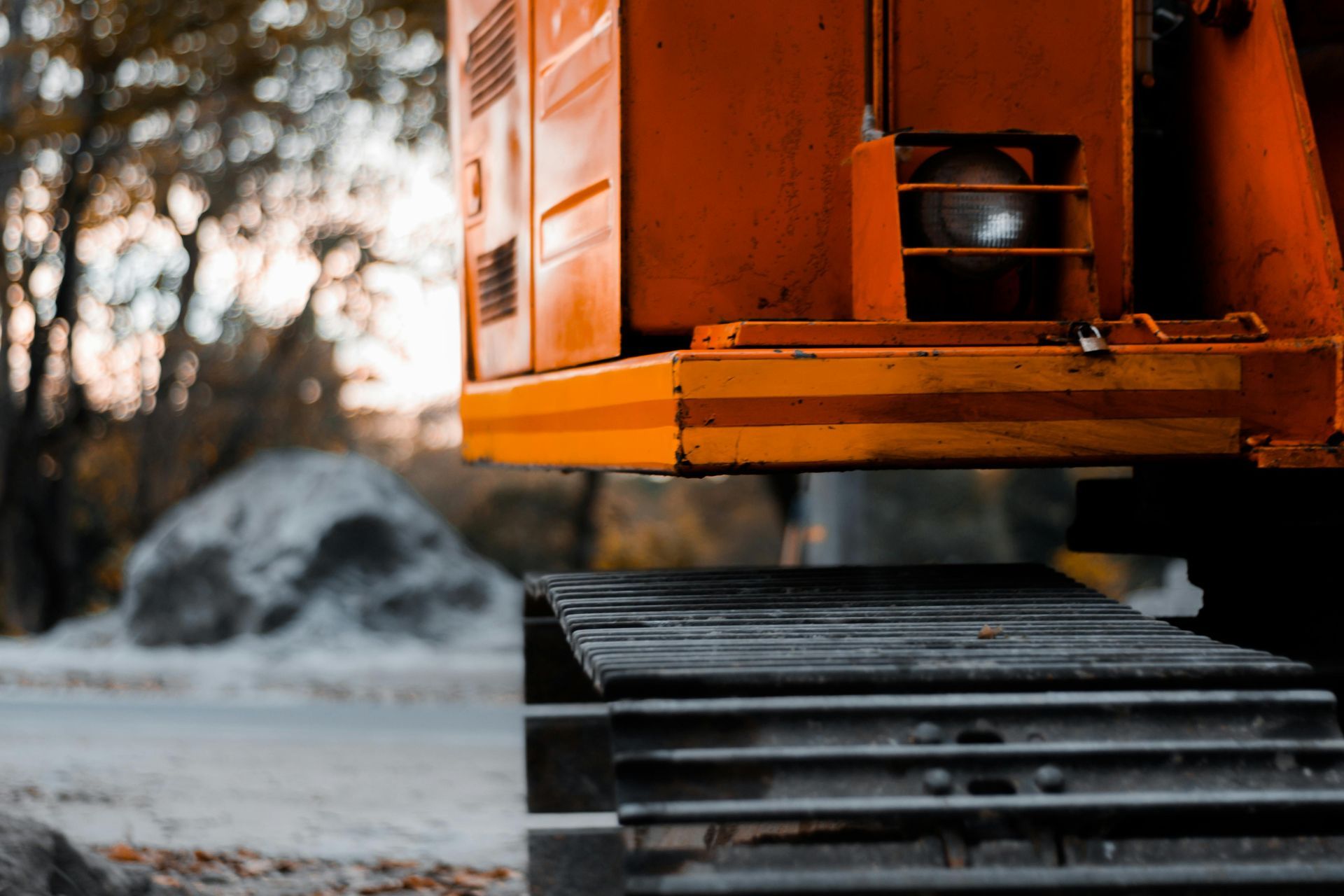 Orange bulldozer, lower section, tracks visible. Blurred background with rocks, trees.