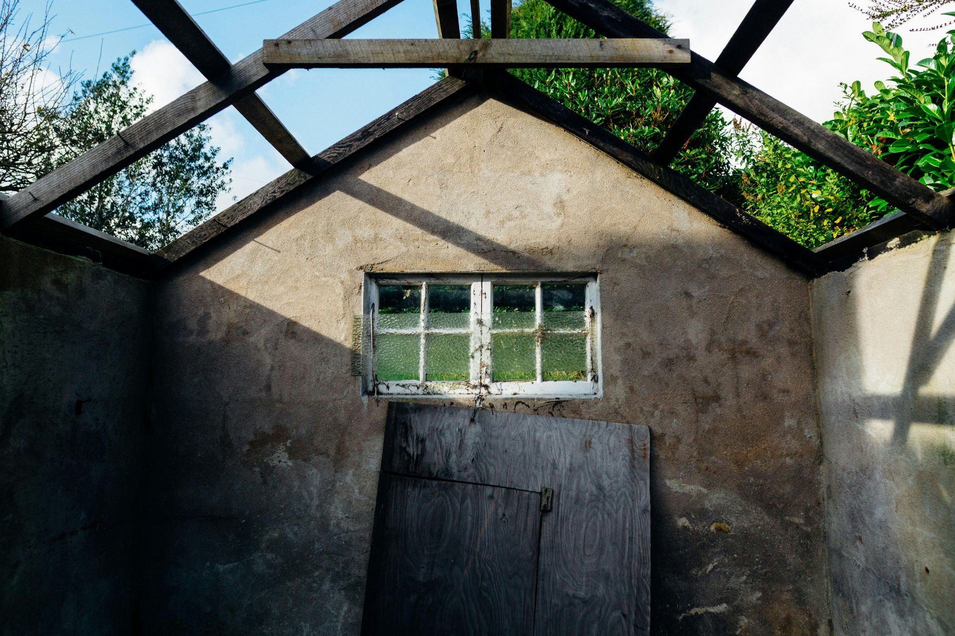 Inside a dilapidated concrete shed with open roof and a small window; a wooden door partially covers the opening.