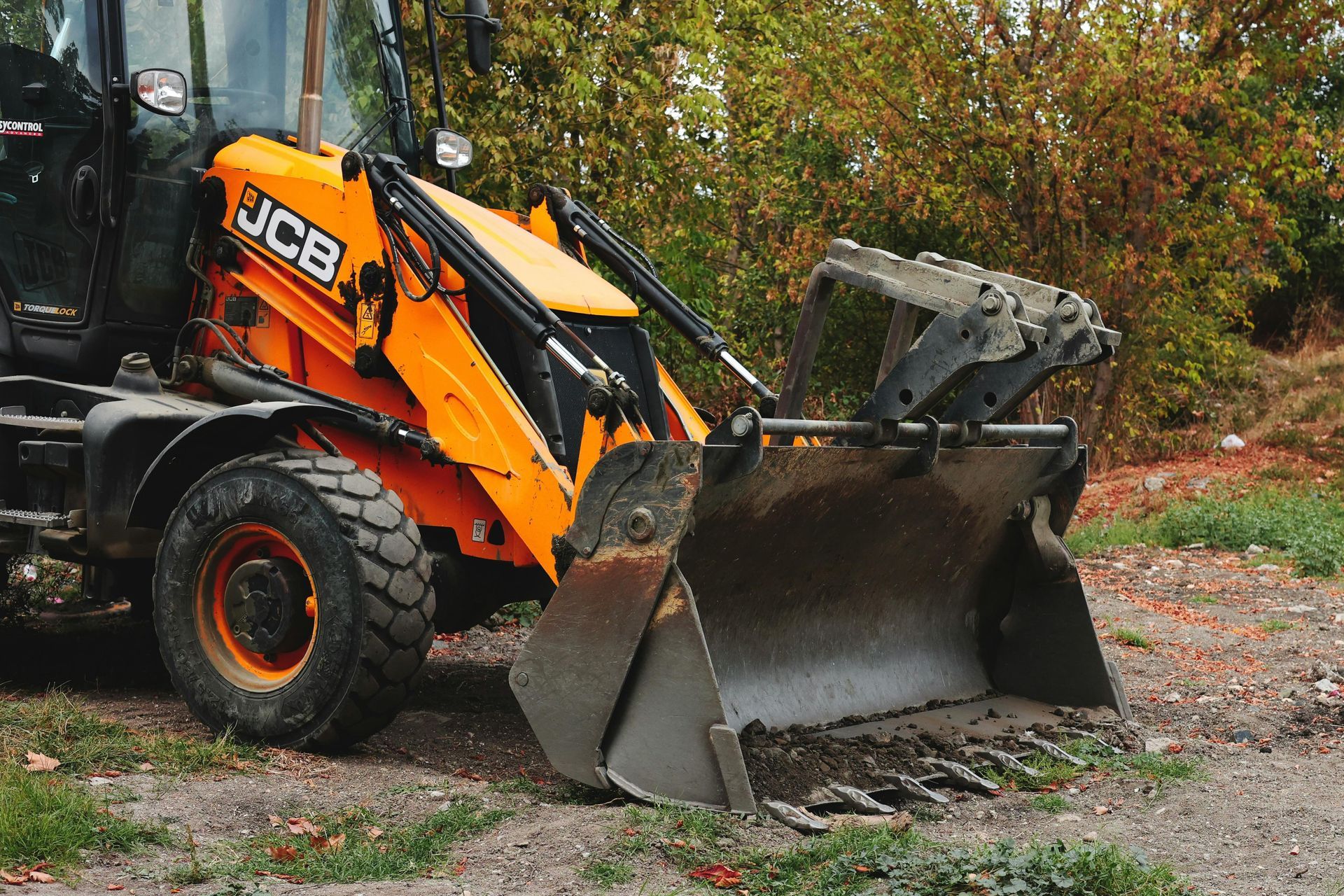 Yellow JCB backhoe loader with raised bucket on gravel.