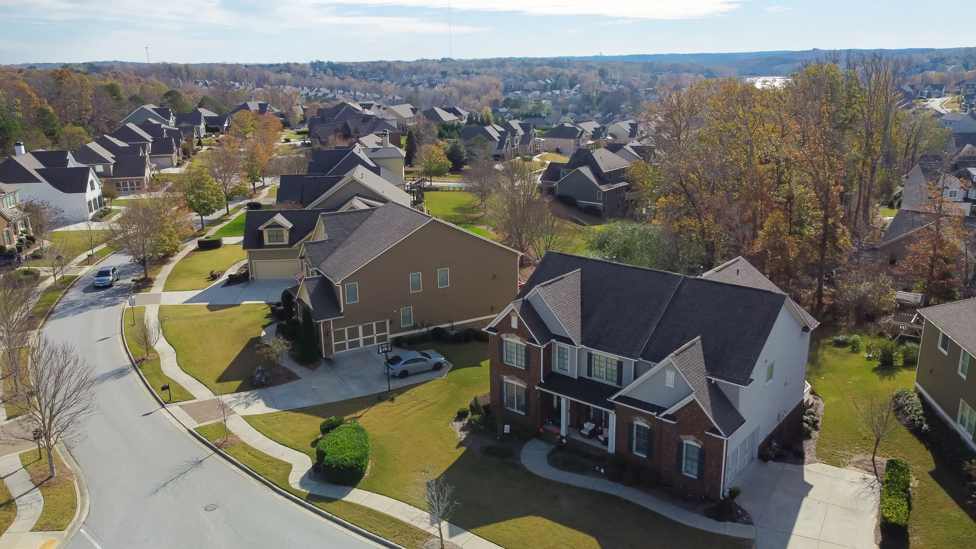 Aerial view of a suburban neighborhood with houses, streets, and autumn foliage under a sunny sky.