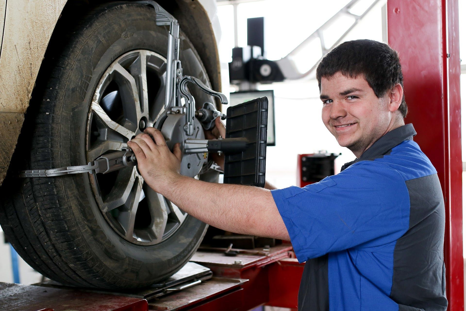 Mechanic using alignment equipment on a car tire, smiling in a garage.