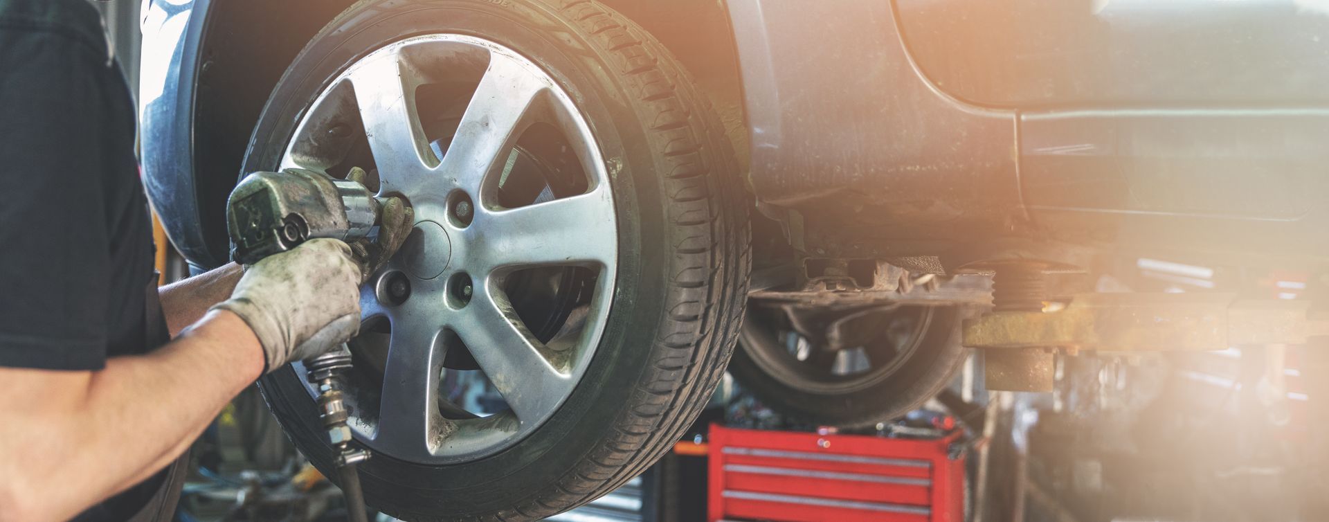 Mechanic uses power tool to remove wheel from car in a shop.