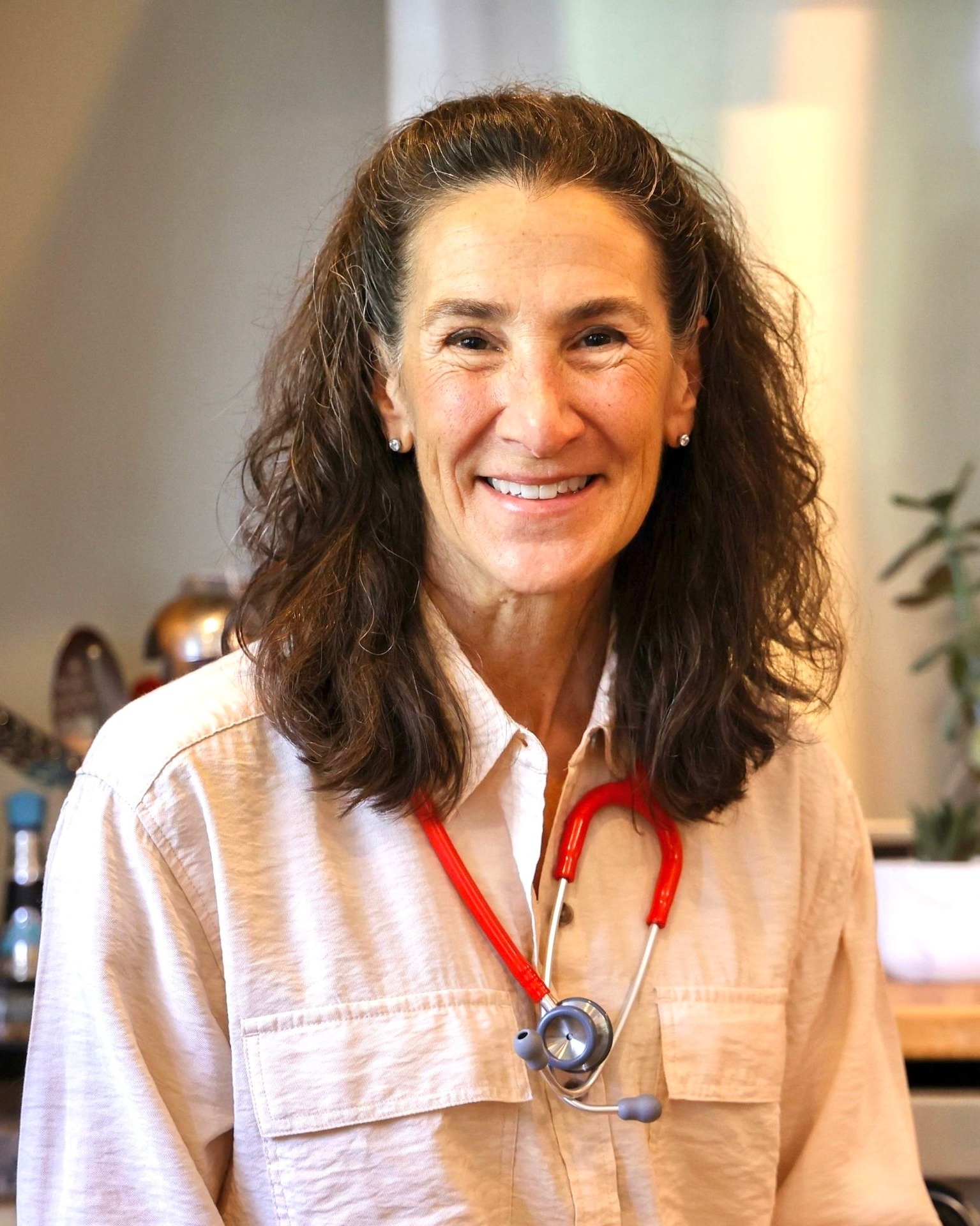 Dr. Bonnie Feola with stethoscope, smiling, wearing tan shirt.