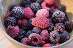 Bowl of frozen mixed berries, including raspberries and blackberries, with frosty coating.
