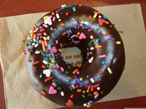 Chocolate glazed donut with colorful sprinkles on a brown napkin.