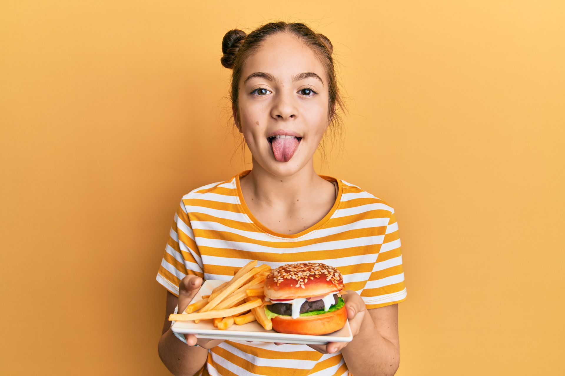 Girl holding a plate with a hamburger and fries, sticking her tongue out.