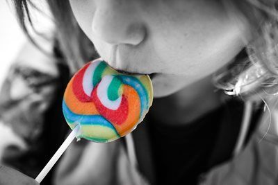 Child's face close to a rainbow-swirled lollipop; child is licking the candy.