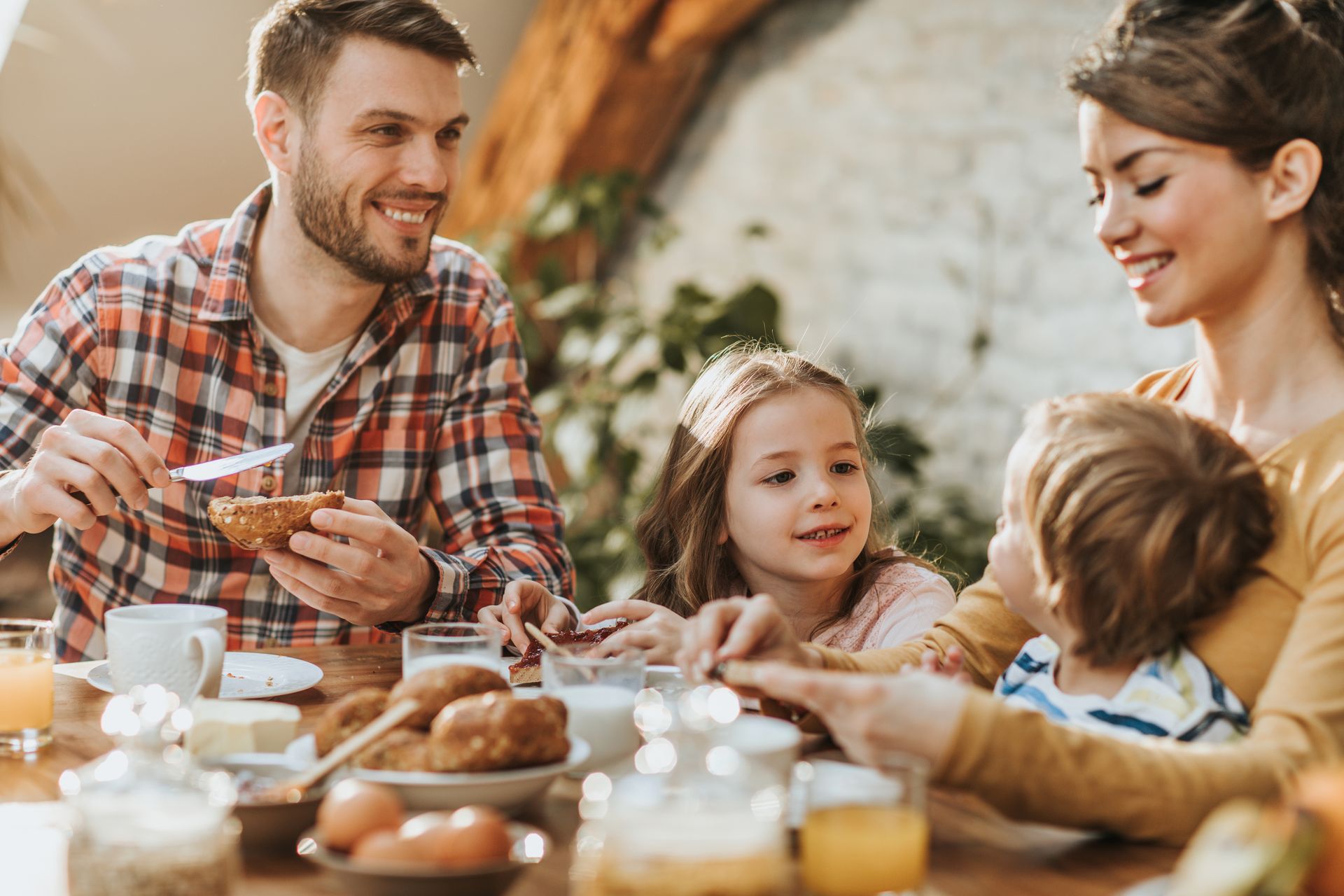 Family enjoying breakfast at a table. Smiling man, woman, and two children. Sunlight streams in.
