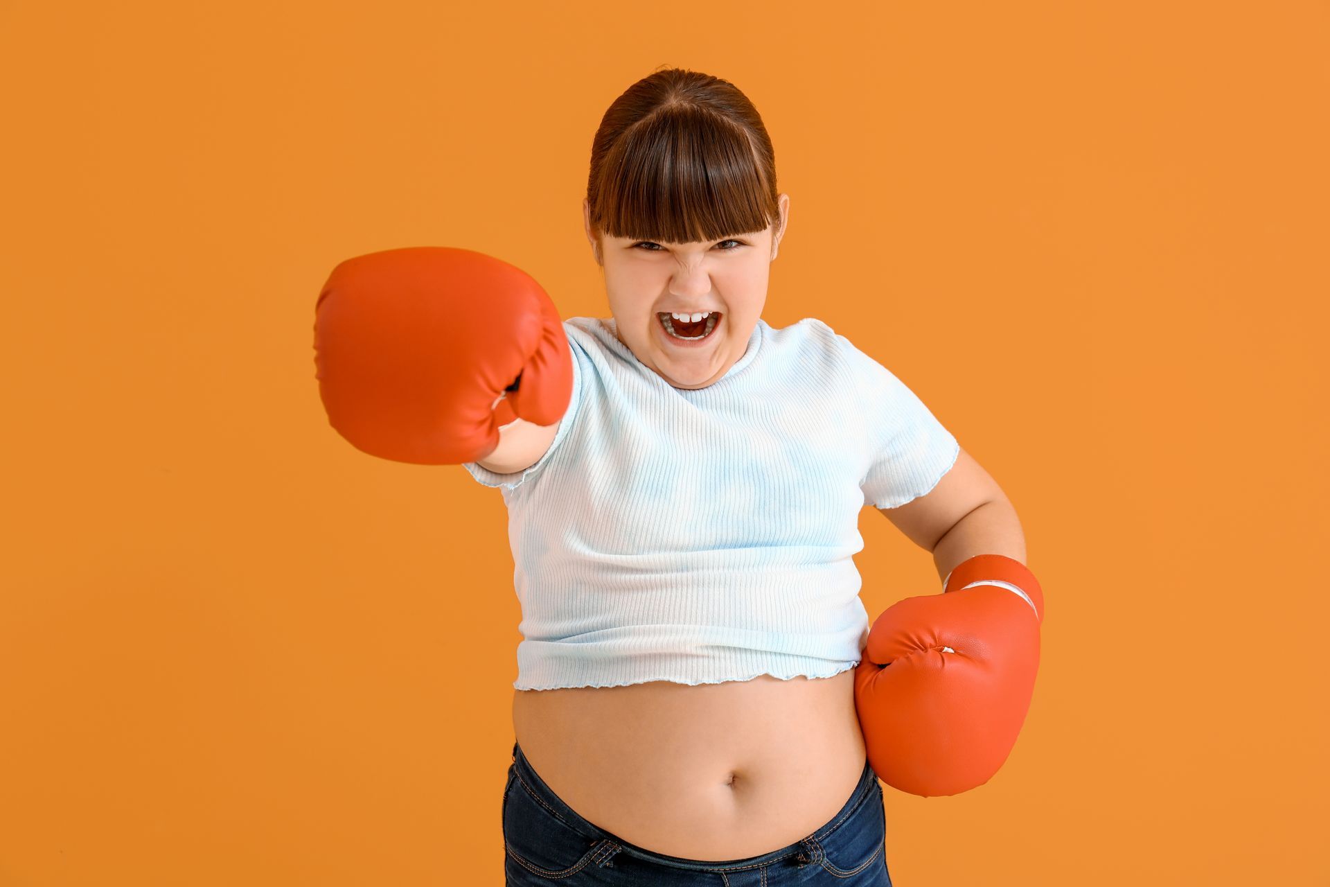 Child with red boxing gloves punches toward camera, orange background.