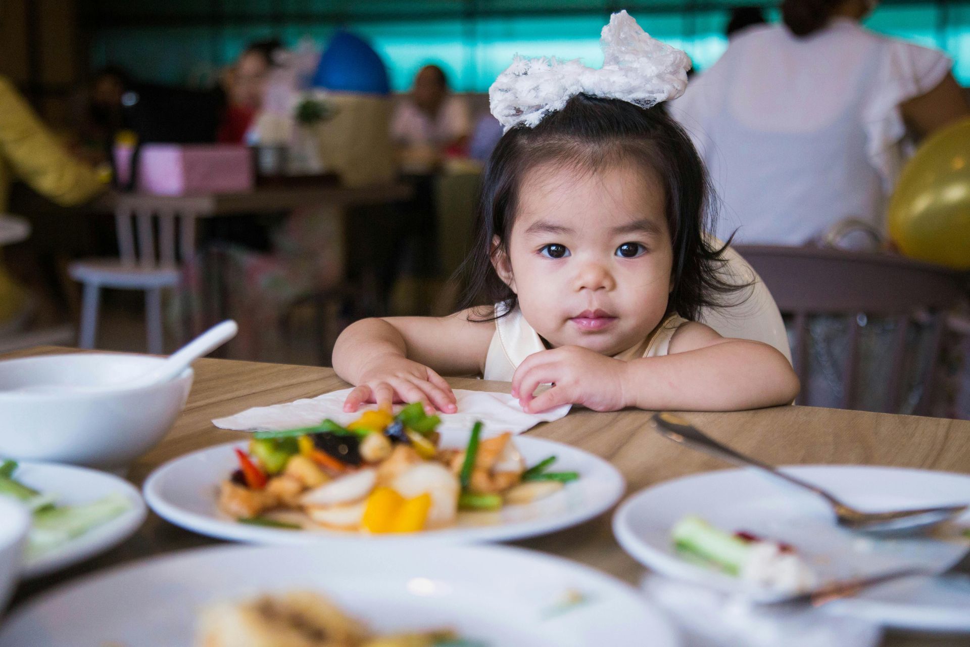A young child at a table with plates of food, looking at the camera.