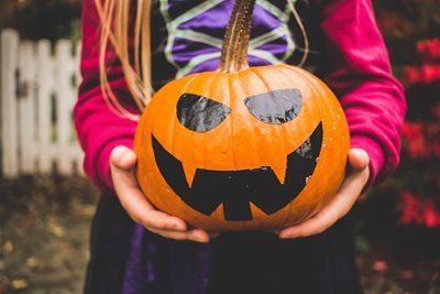 Child holding a carved orange jack-o'-lantern with a black face. Halloween.