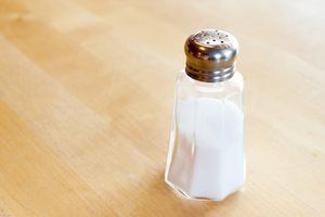 Salt shaker on a wooden table, filled with white salt, silver cap.
