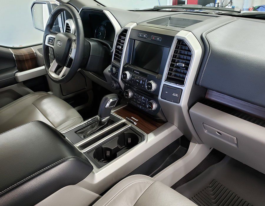 Interior view of a Ford F-150. Black and tan leather seats and dashboard, with a center console and infotainment screen.