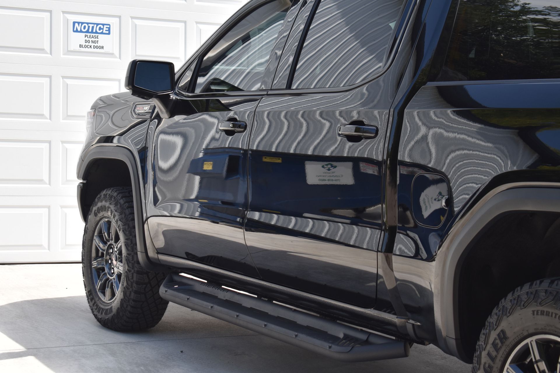 Black pickup truck with running boards parked in front of a white garage door.