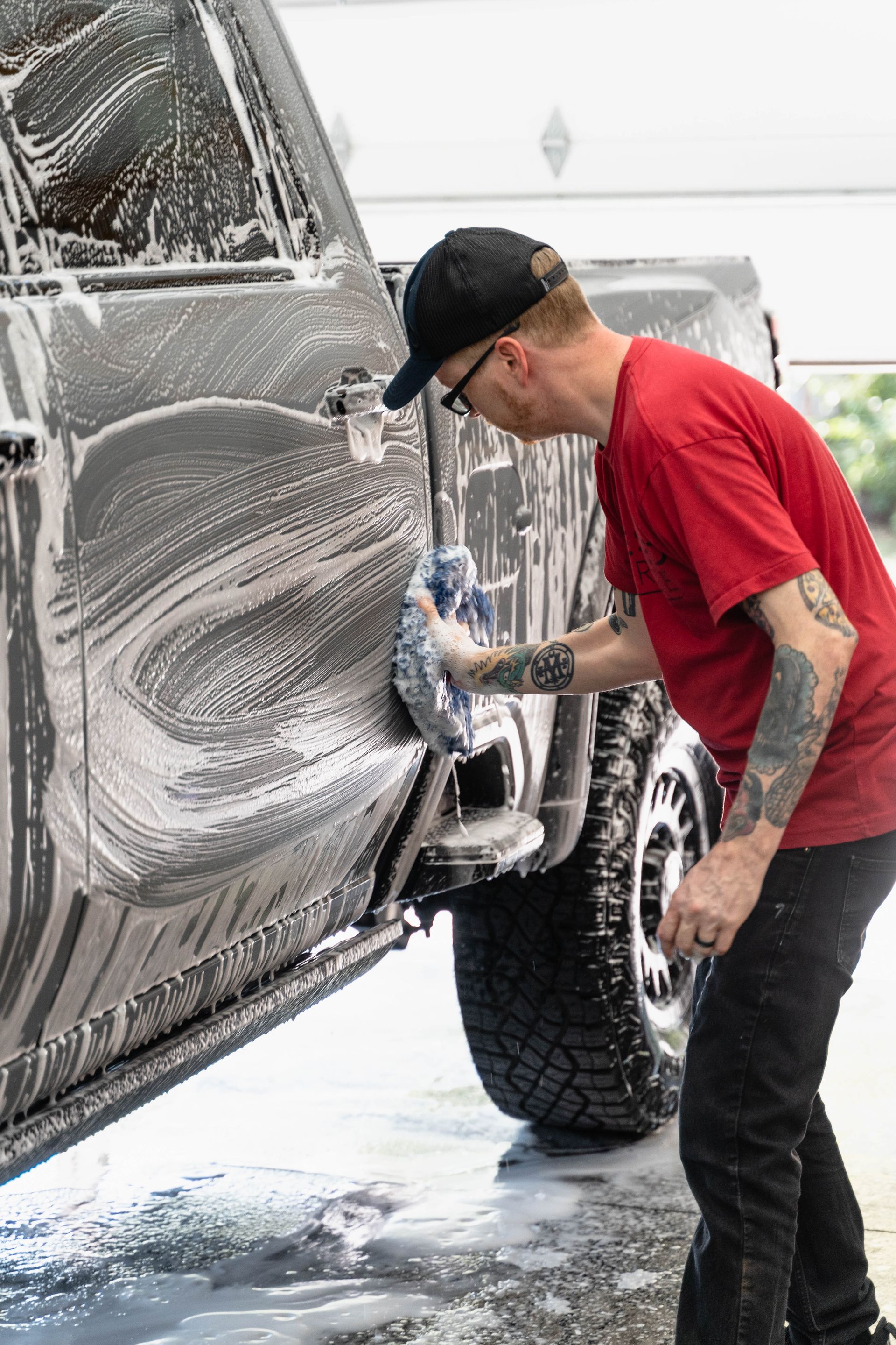 A man in a red shirt is washing a car with foam.