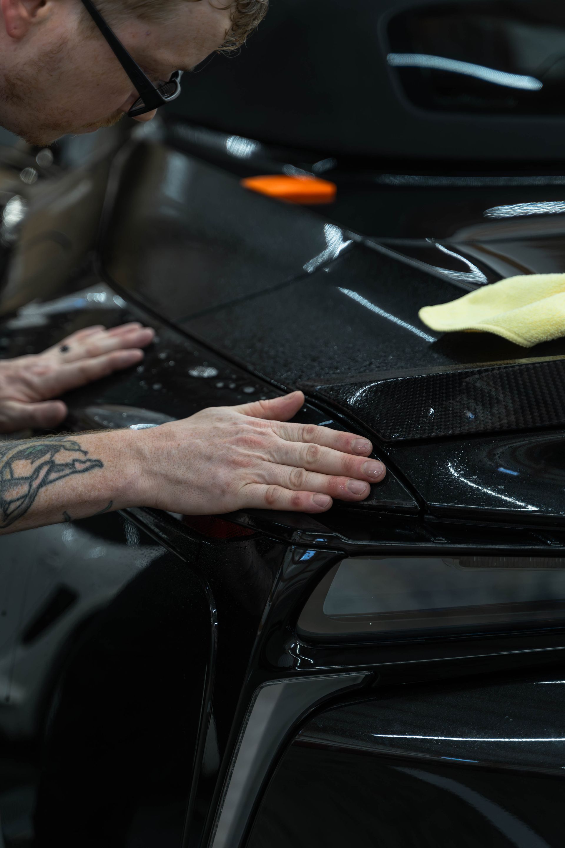 A man is installing paint protection film on the hood of a black car.