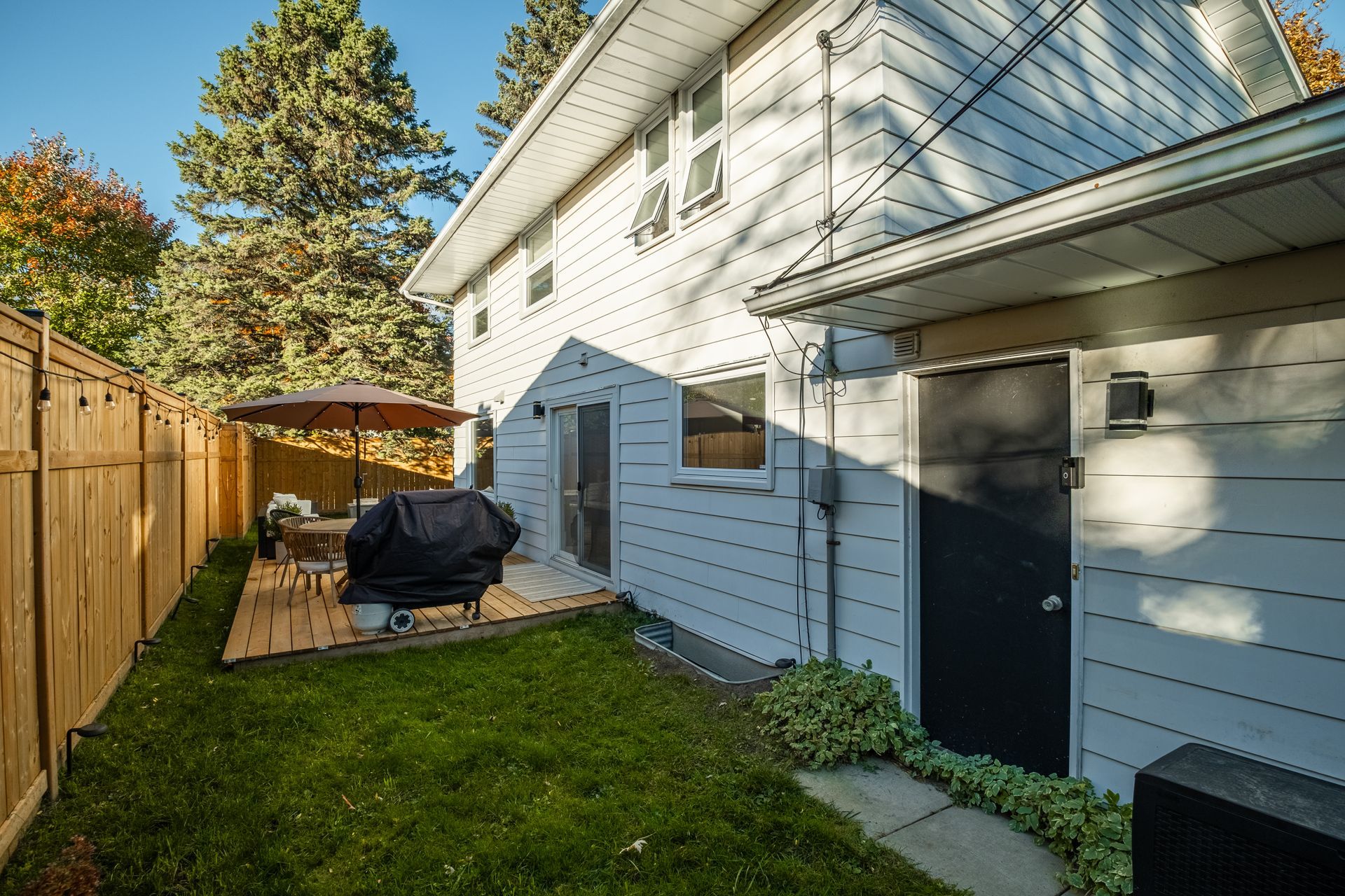 The backyard of a house with a grill and umbrella.