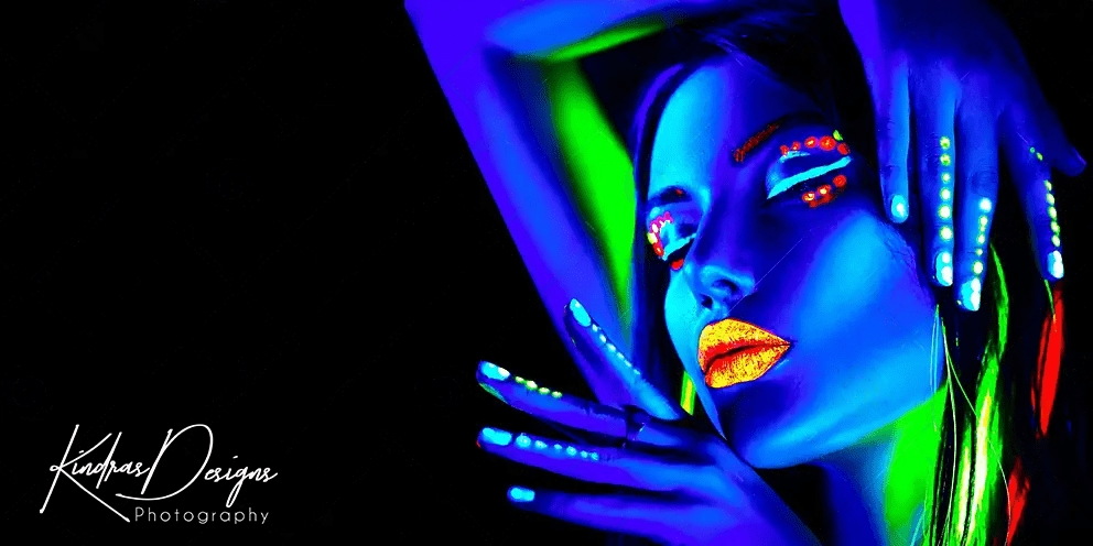 A woman with neon paint on her face and nails is glowing in the dark.
