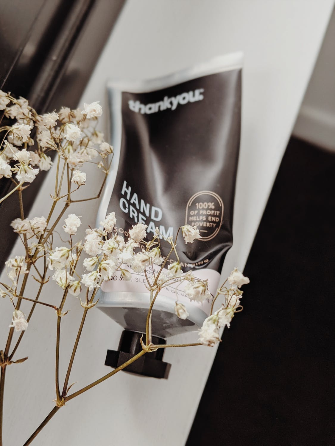 A bottle of hand cream is sitting on a table next to flowers.