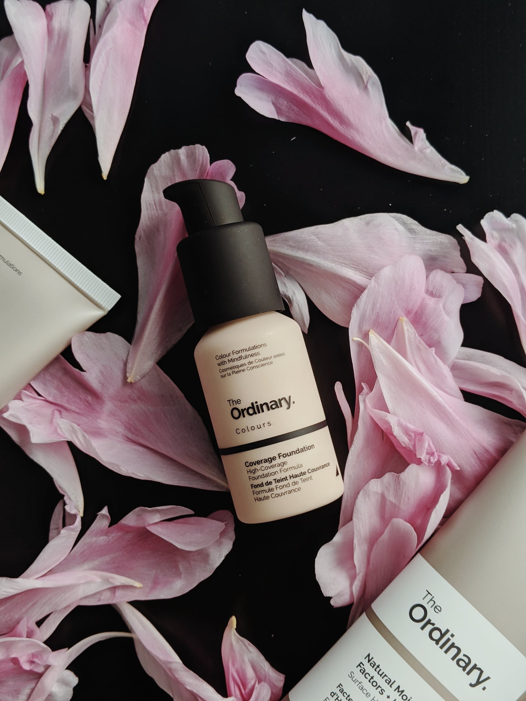 A bottle of the ordinary is surrounded by pink petals