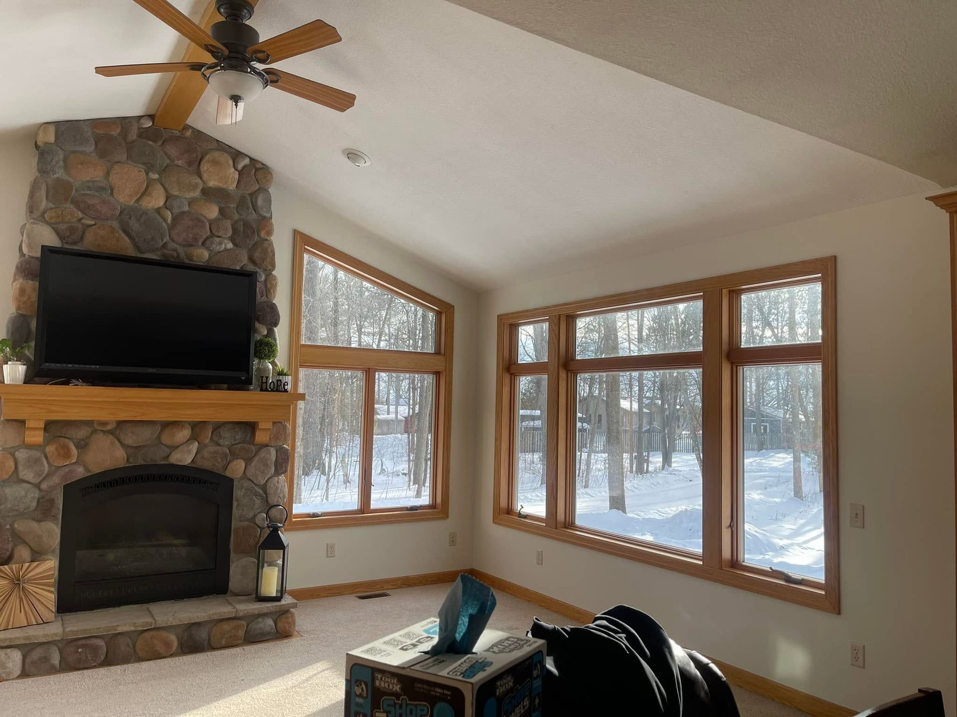 Cozy living room with stone fireplace, large windows, vaulted ceiling, and snowy forest view