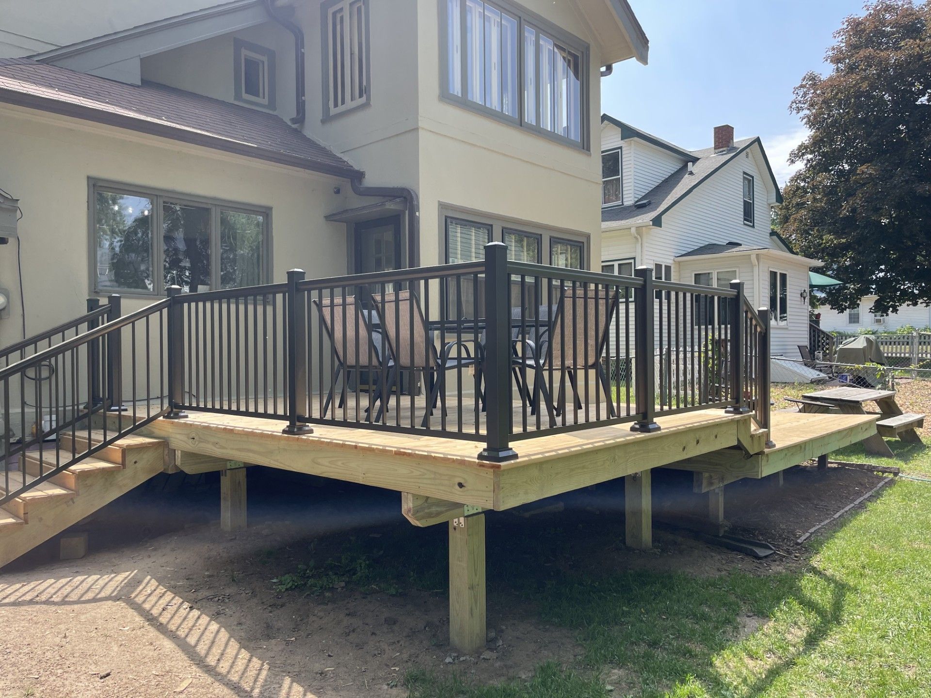 Raised backyard deck with black metal railing beside a house, with stairs and a grassy yard underneath