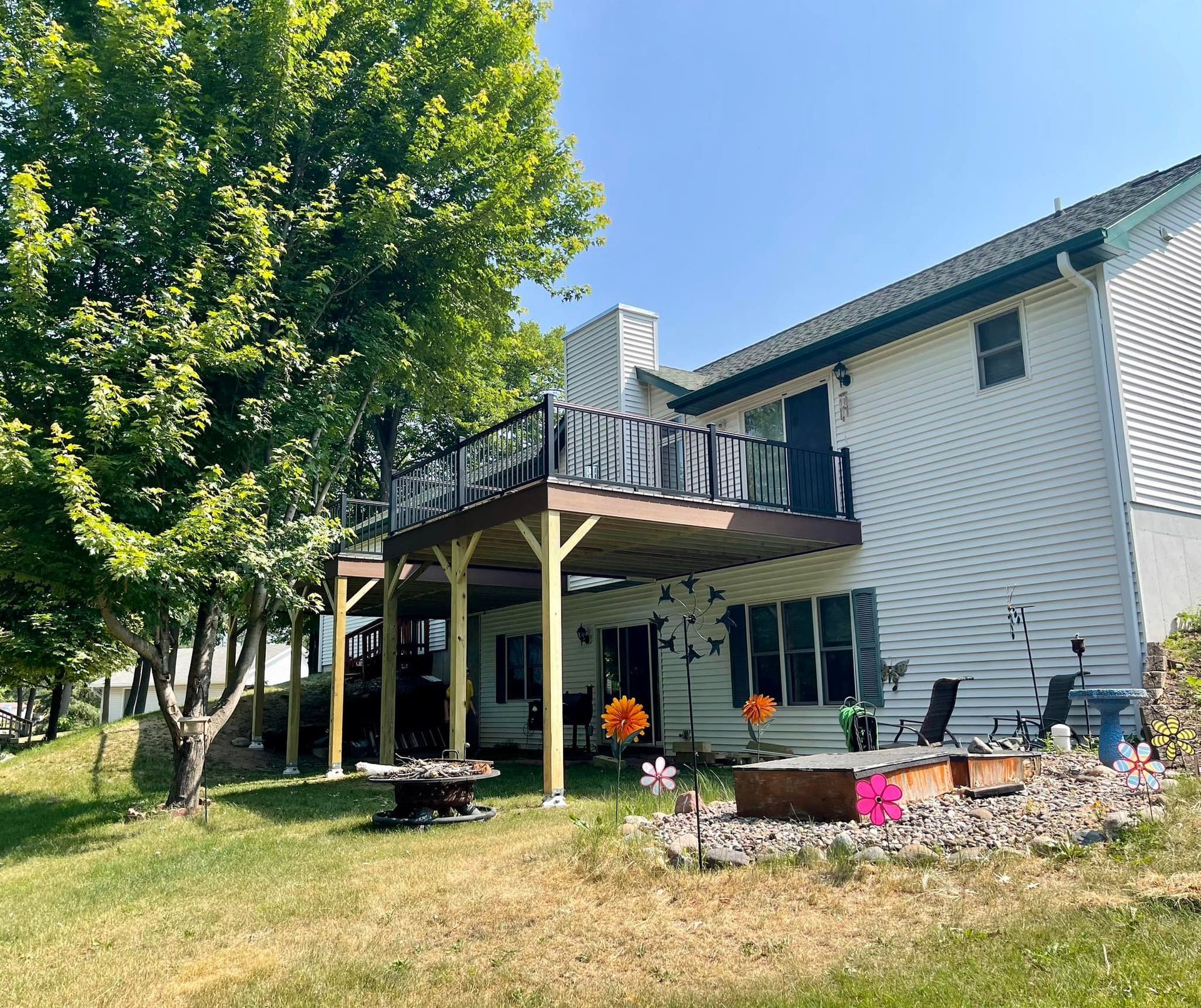 Suburban house with a wooden deck, patio furniture, trees, and a flower bed in the backyard