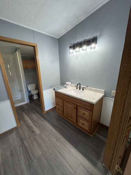 Bathroom vanity with wood cabinet, white sink, gray walls, and wall light above mirrorless countertop.