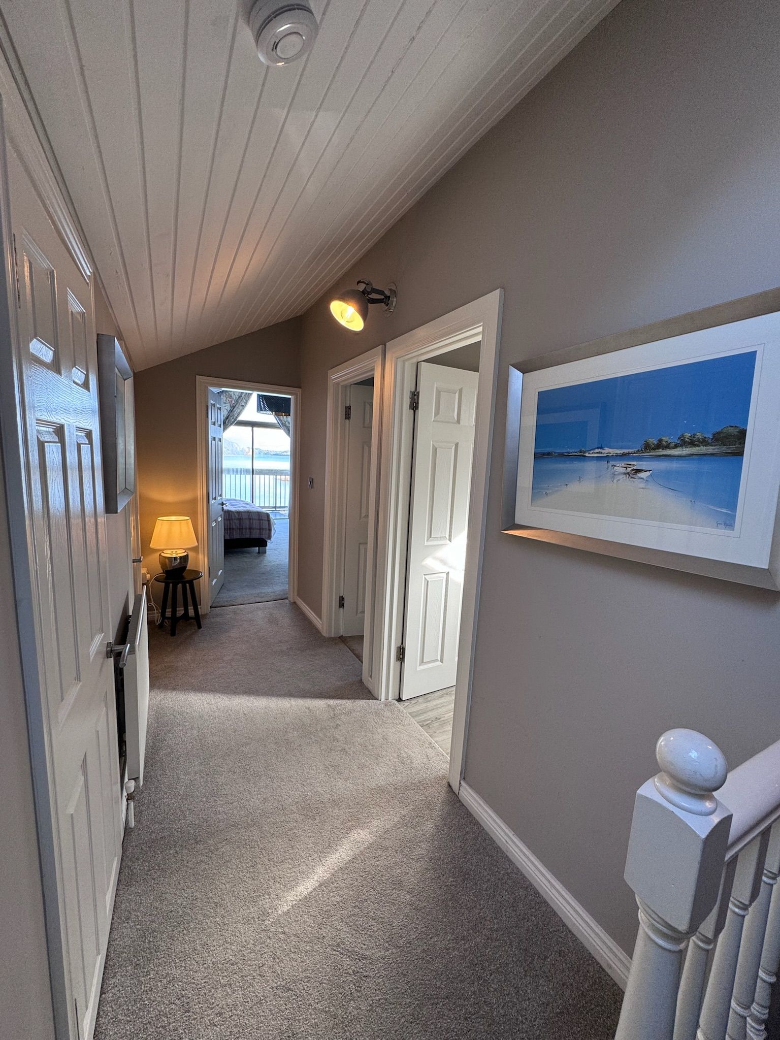 A hallway in a house with a picture of a beach on the wall.